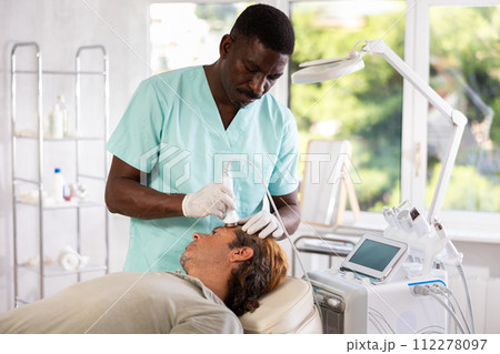 African American esthetician performing anti-aging ultrasonic facial procedure on man African American esthetician performing anti-aging ultrasonic facial procedure on man 112278097