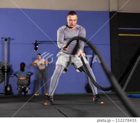 Concentrated man performing battle rope exercise in gym 112278433