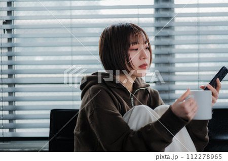 部屋着でソファーに座ってスマホを見る女性 部屋着でソファーに座ってスマホを見る女性 112278965