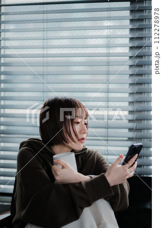 部屋着でソファーに座ってスマホを見る女性 112278978