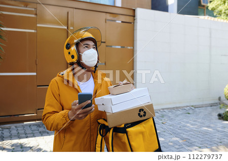 Delivery man in protective mask standing in front of house of customer Delivery man in protective mask standing in front of house of customer 112279737