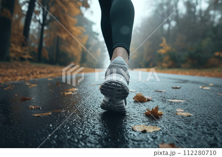 AI-generated content. Legs in sneakers running on wet after rain road with fall yellow leaves in autumn 112280710