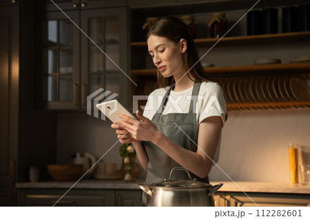 Young Woman in Apron Using Tablet While Cooking in a Modern Kitchen  112282601
