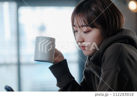 朝部屋でコーヒーを飲みながらスマホを見る女性 112283018