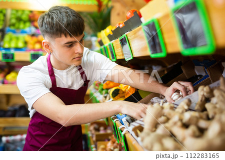 Grocery store employee in an apron puts fresh garlic on shelves Grocery store employee in an apron puts fresh garlic on shelves 112283165