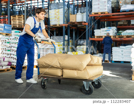 Young guy rolls cart with bags in warehouse 112283407