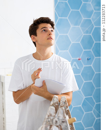 Young designer taking notes on papers while planning interior decoration 112283713