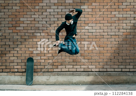 Full length of Asian male fashionable stylish jumping in front of a brick wall 112284138