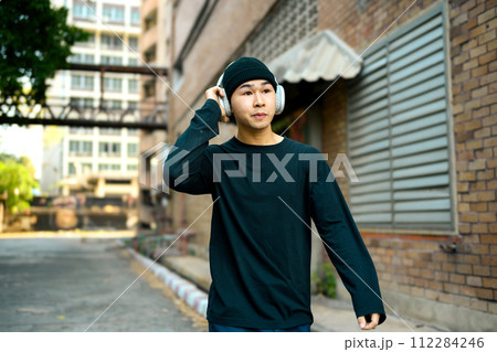 Young male fashionable stylish walking on a city street and listening music with headphones 112284246