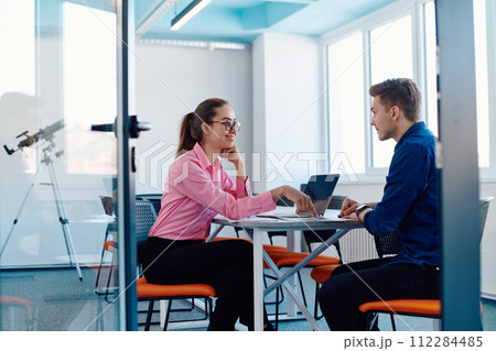In a sleek, modern glass office, the director engages in a productive discussion with an employee, focusing on business projects and fostering collaboration 112284485
