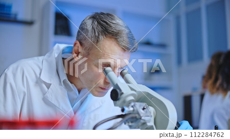 Focused medical technologist looking in microscope, examining blood samples 112284762