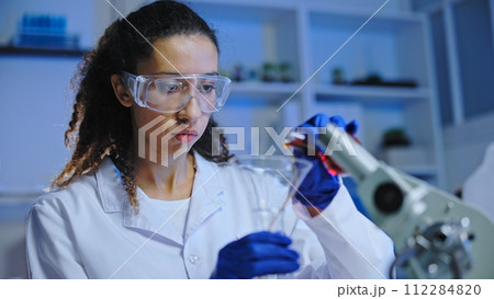 Busy female scientist in protective goggles mixing liquids, conducting laboratory experiment 112284820
