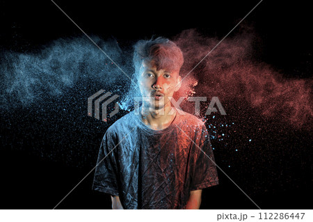 Asian man splashed with colorful holi powder and having fun isolated on black background. 112286447