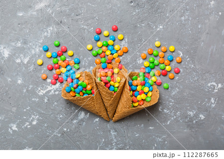 waffle cone full of assorted traditional candies falling out on colored background with copy space. Happy Holidays sale concept 112287665