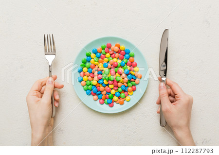 the girl holds cutlery in her hands and eats sweets in a plate. Health and obesity concept, top view on colored background the girl holds cutlery in her hands and eats sweets in a plate. Health and obesity concept, top view on colored background 112287793