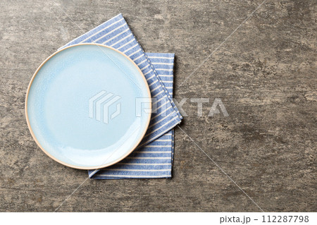 Top view on colored background empty round blue plate on tablecloth for food. Empty dish on napkin with space for your design Top view on colored background empty round blue plate on tablecloth for food. Empty dish on napkin with space for your design 112287798