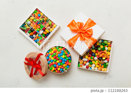 Set of different sweet candy in a paper box with a satin ribbon on a colored background. Holiday concept Set of different sweet candy in a paper box with a satin ribbon on a colored background. Holiday concept 112288263