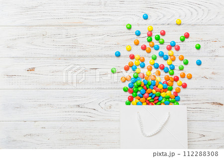 shopping paper gift bag in corner full of assorted traditional candies falling out on colored background with copy space. Happy Holidays sale concept shopping paper gift bag in corner full of assorted traditional candies falling out on colored background with copy space. Happy Holidays sale concept 112288308