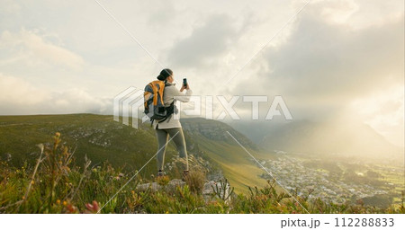 Woman, trekking and video recording on mountains in adventure, wellness and health with nature and cityscape. Person with backpack and hiking photography on green hill, travel or eco friendly journey 112288833