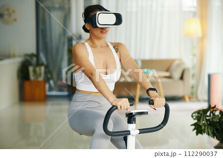 Fit woman wearing virtual reality headset when riding exercise bike Fit woman wearing virtual reality headset when riding exercise bike 112290037