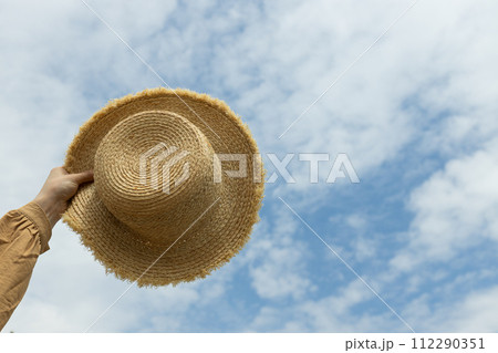 A straw hat in his hand, against the background of the sky. 112290351