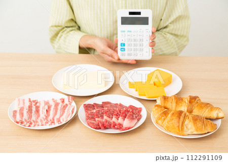 脂質を多く含む食品と電卓を持つ女性 112291109