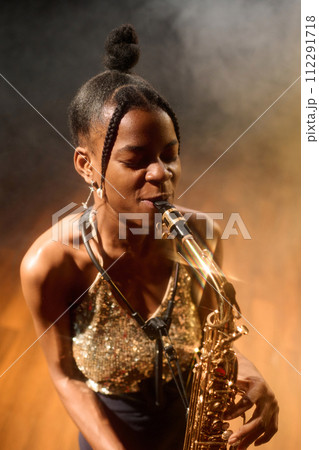 Vertical portrait of passionate Black young woman playing saxophone music in jazz club Vertical portrait of passionate Black young woman playing saxophone music in jazz club 112291718