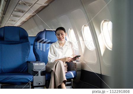 Traveling and technology. Flying at first class. Young business woman passenger using smartphone while sitting in airplane flight Traveling and technology. Flying at first class. Young business woman passenger using smartphone while sitting in airplane flight 112291808