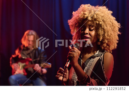 Waist up portrait of young African American woman with real hair texture singing into microphone on stage in nightclub copy space 112291852