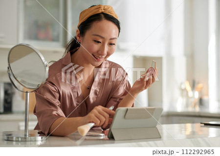 Smiling woman following tutorial on tablet computer when doing makeup 112292965