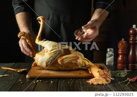 Adding dry spices to raw rooster. Chef preparing chicken on kitchen table for delicious lunch in restaurant 112293025