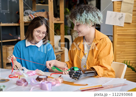 Portrait of two teenage girls enjoying sewing class in inclusive training center and holding ribbons with prosthetic hands Portrait of two teenage girls enjoying sewing class in inclusive training center and holding ribbons with prosthetic hands 112293068