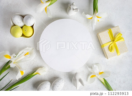 Easter layout. Decorative eggs, iris flowers, gift box, bunnies around round blank space on white. Easter layout. Decorative eggs, iris flowers, gift box, bunnies around round blank space on white. 112293913