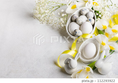 Easter festive card with eggs in plates with bunny ears, small bunnies, flowers on white. Copy space 112293922