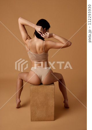 Rear view of woman in beige lingerie, highlighting back muscles and comfortable underwear fit against sandy color studio background. Rear view of woman in beige lingerie, highlighting back muscles and comfortable underwear fit against sandy color studio background. 112293930