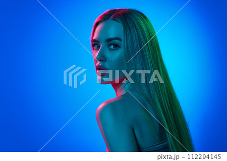 Portrait of young blonde beautiful woman with perfect smooth skin against blue studio background in neon light. Self-care Portrait of young blonde beautiful woman with perfect smooth skin against blue studio background in neon light. Self-care 112294145