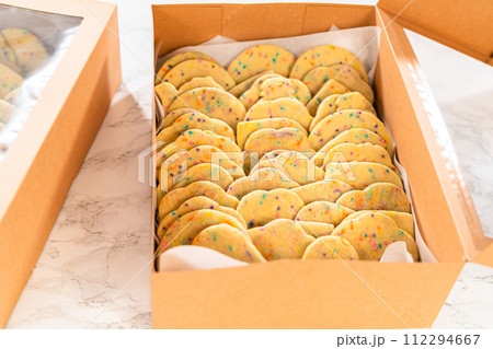 The sugar cookies, filled with sprinkles mixed into the dough, are carefully arranged with meticulous precision into a rustic brown paper box. The sugar cookies, filled with sprinkles mixed into the dough, are carefully arranged with meticulous precision into a rustic brown paper box. 112294667