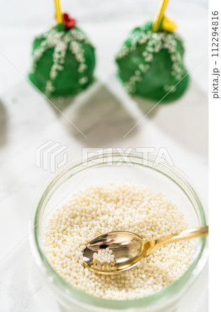 Decorating cactus cake pops with luster dust, sugar glower, and white sprinkles for the Cinco de Mayo celebration. Decorating cactus cake pops with luster dust, sugar glower, and white sprinkles for the Cinco de Mayo celebration. 112294816
