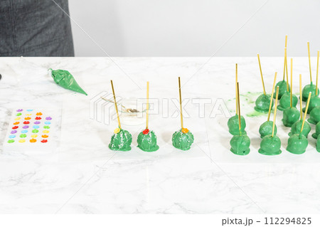 Decorating cactus cake pops with luster dust, sugar glower, and white sprinkles for the Cinco de Mayo celebration. Decorating cactus cake pops with luster dust, sugar glower, and white sprinkles for the Cinco de Mayo celebration. 112294825