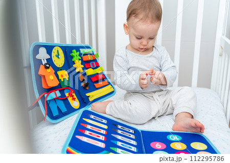 Baby playing with montessori busy book sitting in crib. Concept of smart books and modern toys Baby playing with montessori busy book sitting in crib. Concept of smart books and modern toys 112295786
