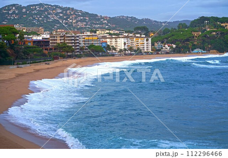 Fenals Beach, Lloret de Mar Spain. Top view of a deserted beach in cloudy weather, blue, turquoise, thick water, green vegetation, storm at sea. Mediterranean, transparent, nature, tourism of European Fenals Beach, Lloret de Mar Spain. Top view of a deserted beach in cloudy weather, blue, turquoise, thick water, green vegetation, storm at sea. Mediterranean, transparent, nature, tourism of European 112296466