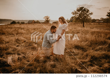 husband hugs pregnant wife hold hands on big round tummy kissing belly. 112298574