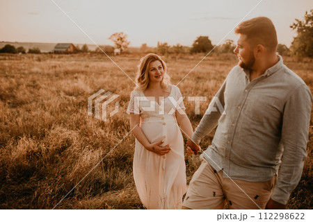 Happy family pregnant caucasian blonde woman walks with husband in meadow in summer. 112298622