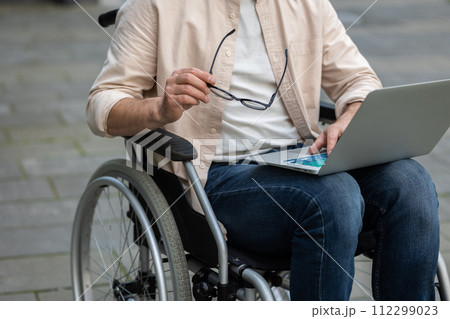 Disabled self-employed man working on laptop while sitting in wheelchair in hospital yard Disabled self-employed man working on laptop while sitting in wheelchair in hospital yard 112299023
