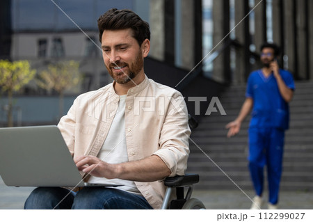 Disabled self-employed man working on laptop while sitting in wheelchair in hospital yard 112299027