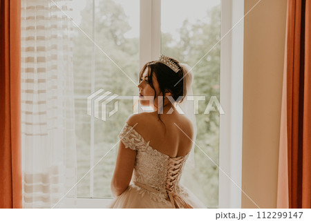 woman bride in white wedding dress girl stands with her back near window morning 112299147