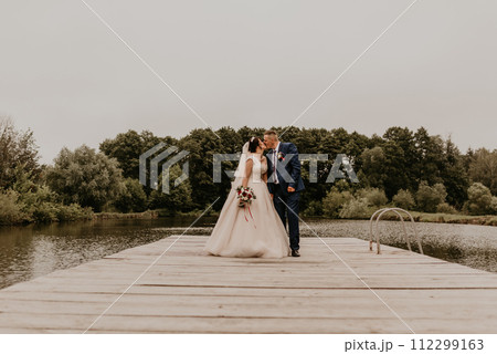 Newlyweds kissing hugging on wooden pier bridge on lake 112299163