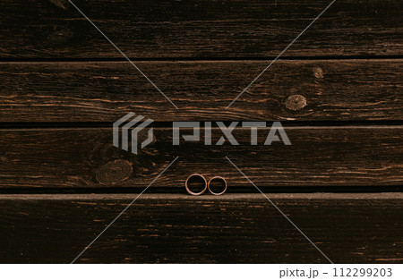 pair gold wedding engagement precious expensive rings placed on dark brown wooden striped timber plank background pair gold wedding engagement precious expensive rings placed on dark brown wooden striped timber plank background 112299203