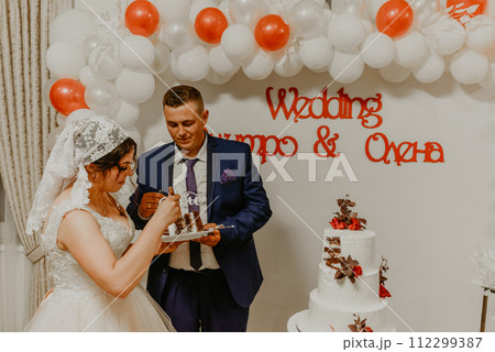 groom and bride at wedding cut their large multi-tiered white cake taste it fed from each other. groom and bride at wedding cut their large multi-tiered white cake taste it fed from each other. 112299387