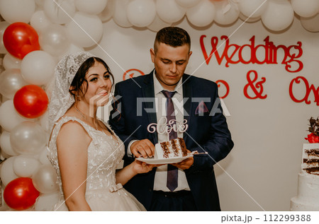 groom and bride at wedding cut their large multi-tiered white cake taste it fed from each other. 112299388